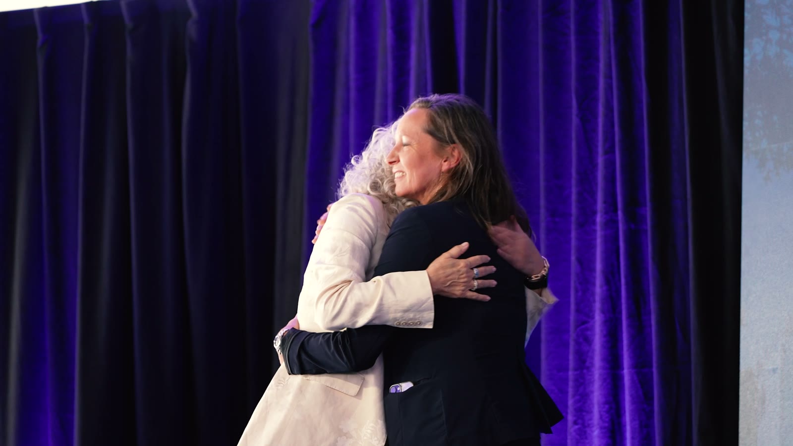 Deux collaboratrices se saluent devant les rideaux violets du chapiteau, avant la plénière