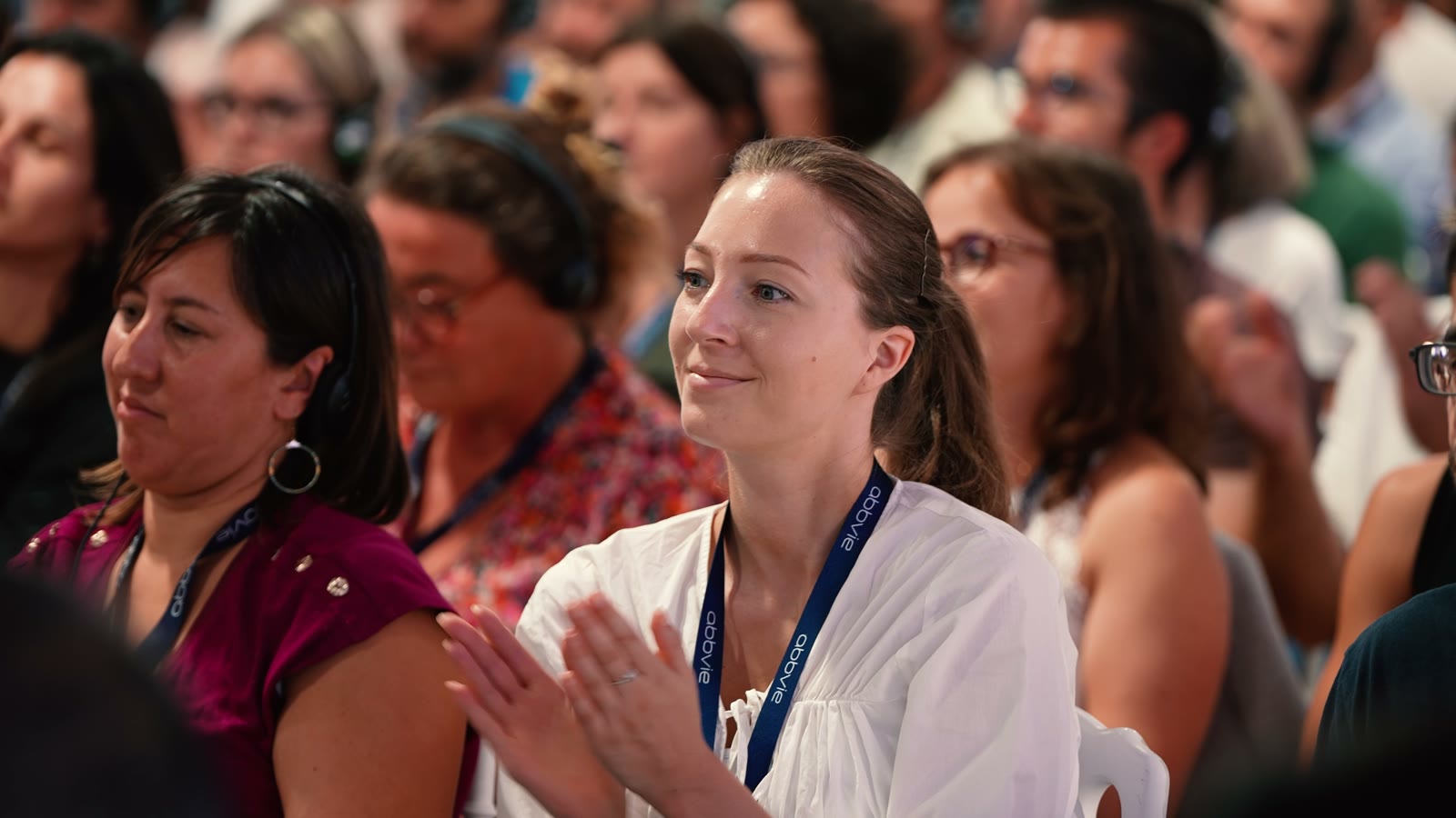 Participantes souriantes dans le public de la plénière, badges autour du cou
