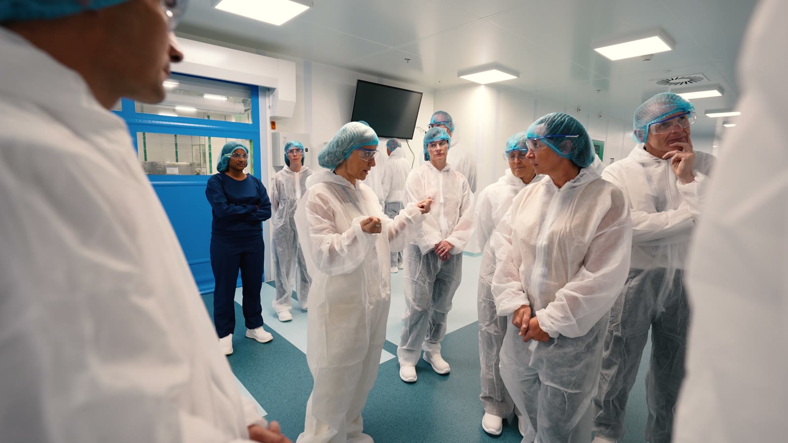 Visiteurs en combinaisons blanches et charlottes dans un couloir de salle blanche du site AbbVie