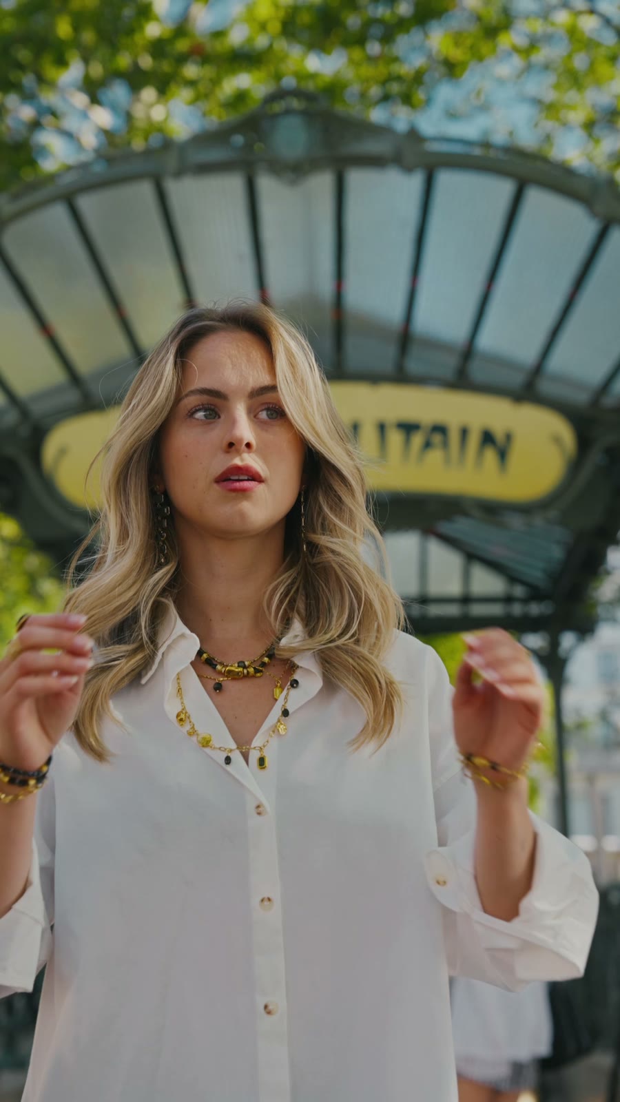 Camille en chemise blanche devant l'entrée Guimard du métro Abbesses, sautoirs et bracelets dorés Eiden